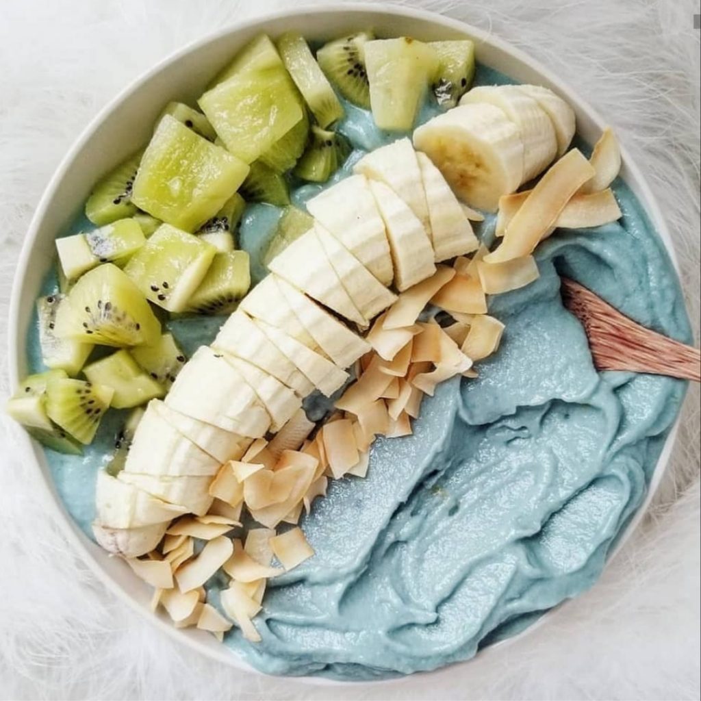 thick blue smoothie bowl topped with banana, coconut, and kiwi
