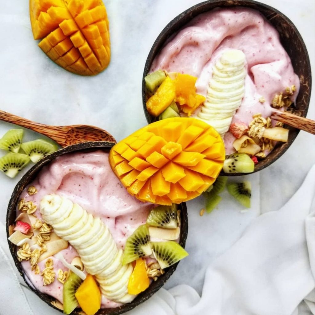 strawberry pineapple smoothie bowl in a coconut bowl topped with fresh tropical fruit