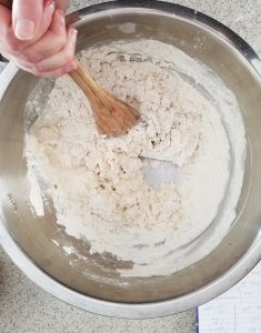 stainless steel bowl with the ciabatta roll dough inside. Mixing the dough with a wooden spoon 