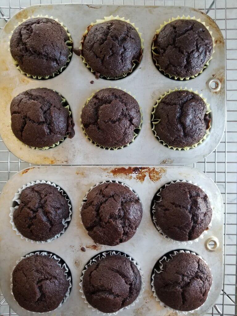 dairy free banana chocolate muffins in muffin tins on a stainless steel cooling rack