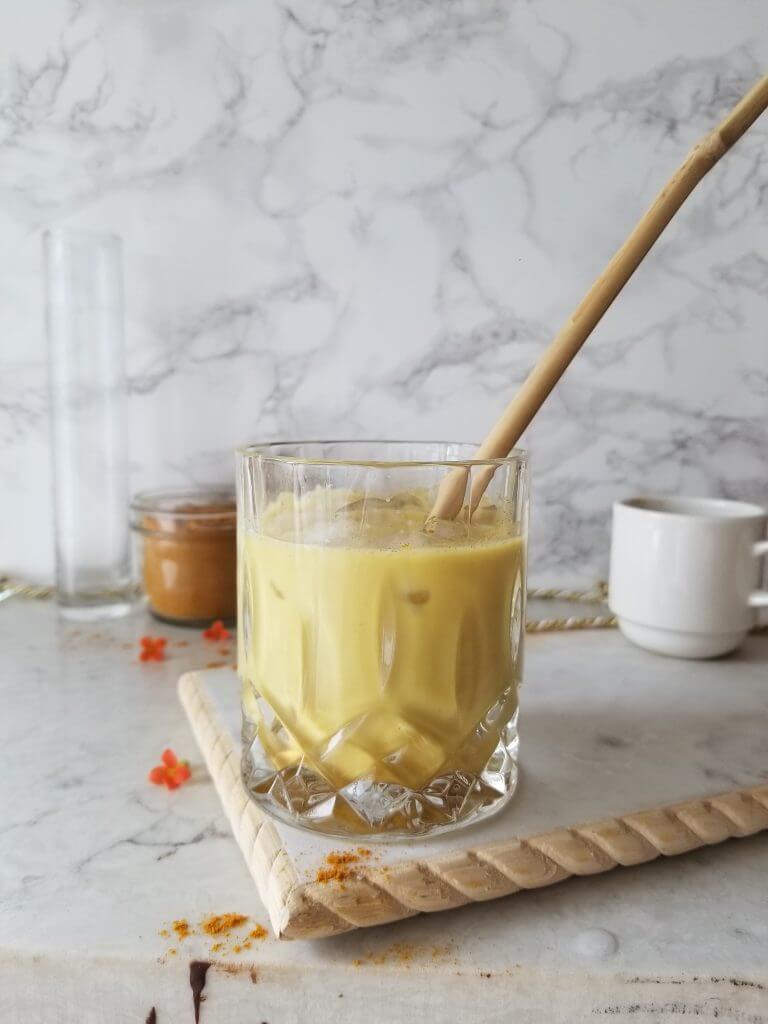 iced golden milk latte in a crystal glass with golden milk latte mix in the background 