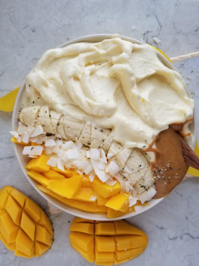 pineapple banana smoothie in a white bowl topped with banana, coconut chips, mango, and peanut butter
