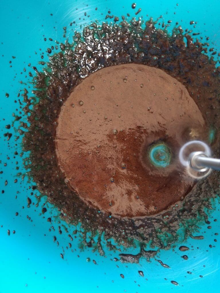 continuing to whip the coffee with a blender in a blue bowl 