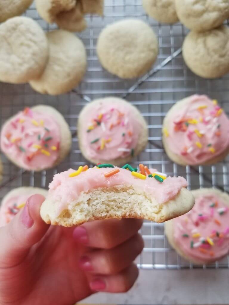 bite shot of a pink frosted sugar cookie with rainbow sprinkles