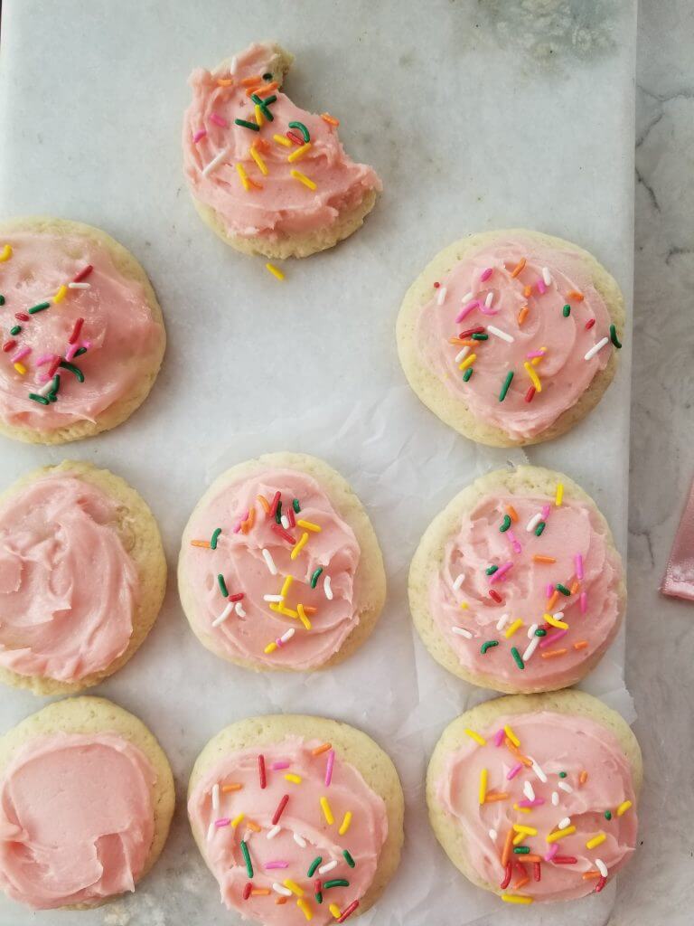 pink frosted sugar cookies with rainbow sprinkles on white marble board