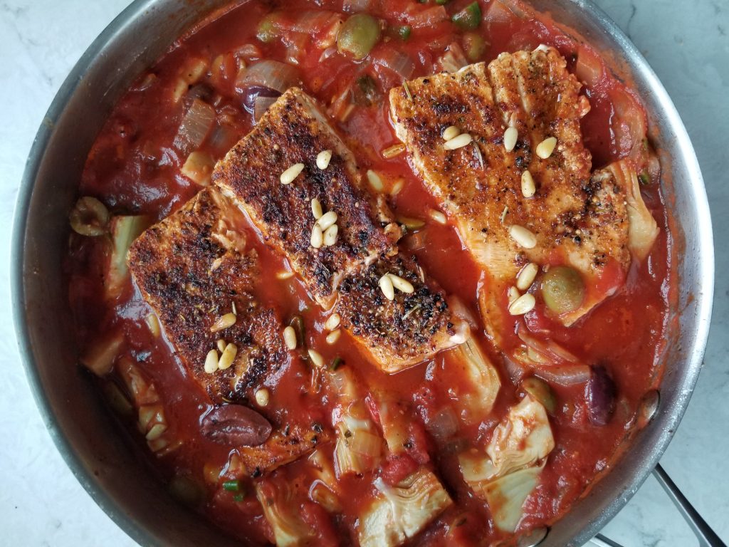 cooked Arabic salmon in a pan of tomato sauce with toasted pine nuts