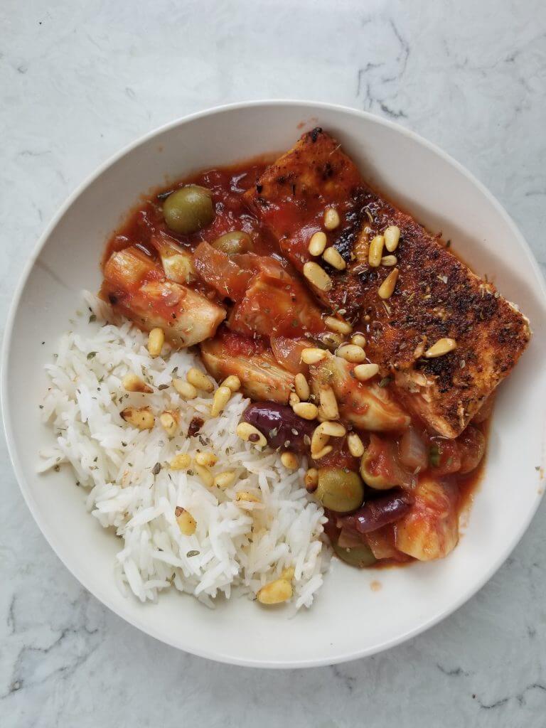 bowl of tomato artichoke sauce with crispy Arabic salmon and rice topped with pine nuts