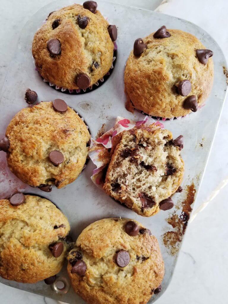 dairy free banana chocolate chip muffins in a muffin tin showing one cut in half for its texture 