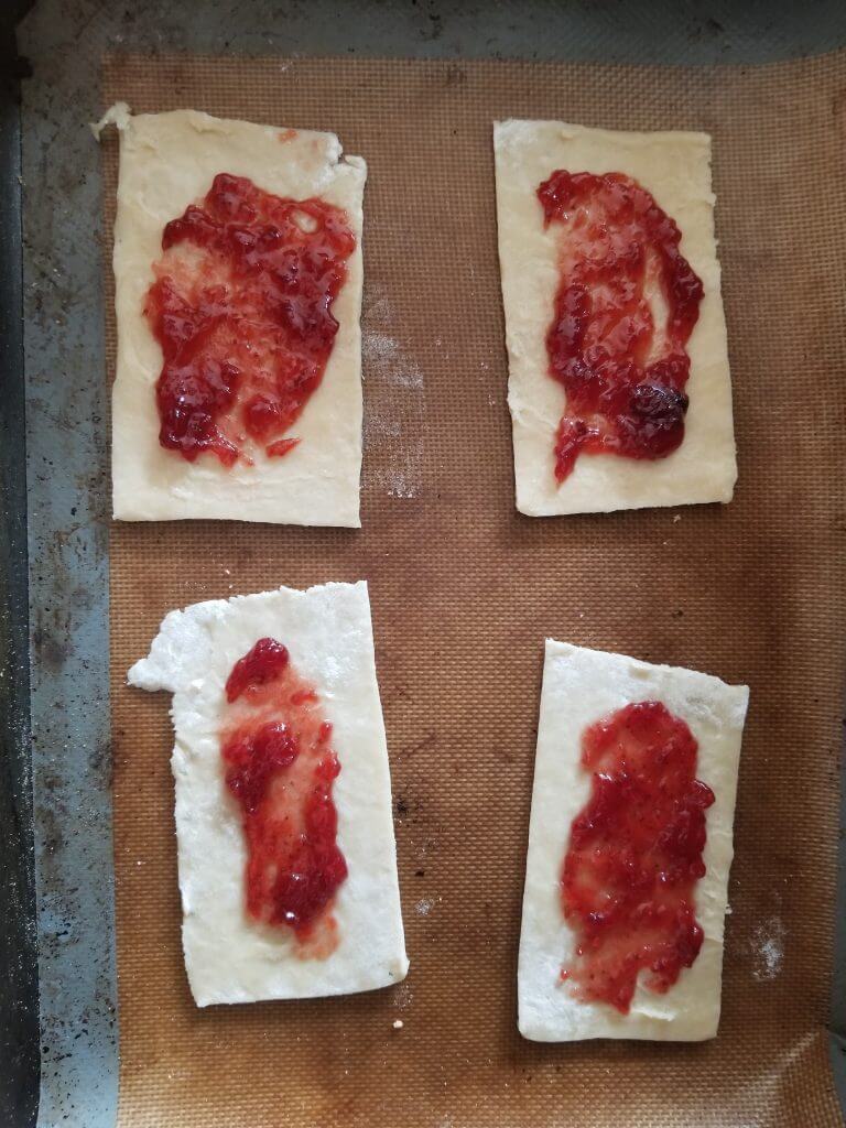 Bottom half of the pop tarts on a baking tray with jam added to them 