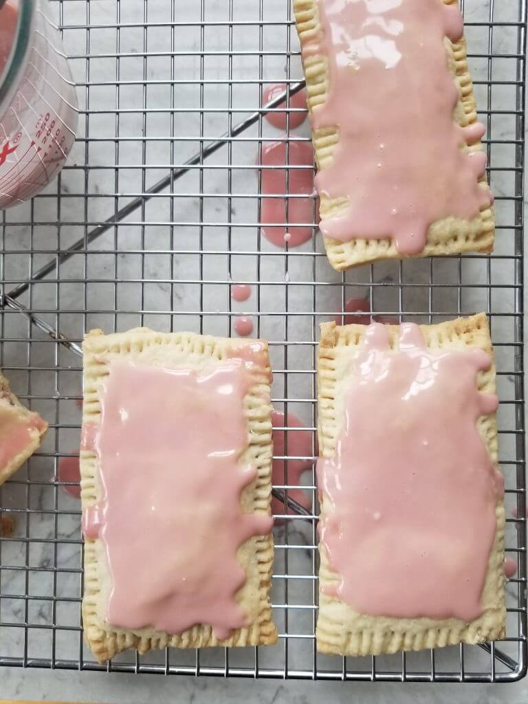 pop tarts with pink glaze added on top on a cooling rack 