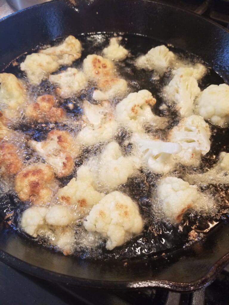 cauliflower frying in a cast iron skillet of oil