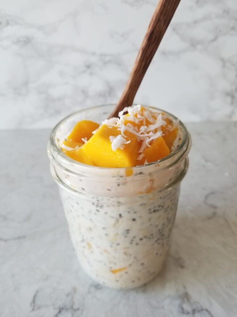 tropical mango overnight oats in a mason jar with fresh mango and coconut on top 
