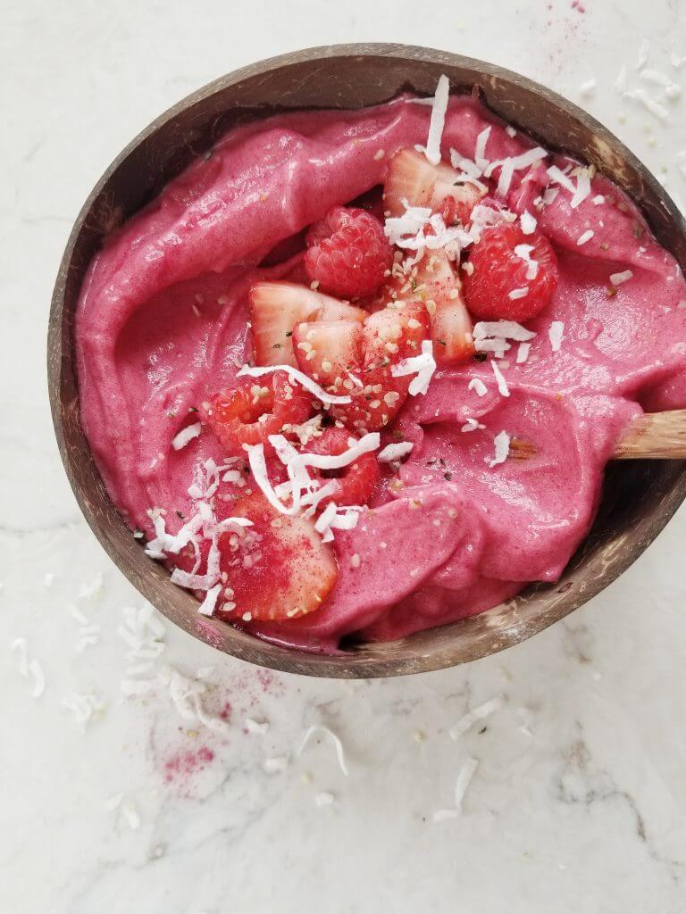 strawberry banana smoothie bowl in a coconut bowl topped with strawberries, coconut, and hemp seeds