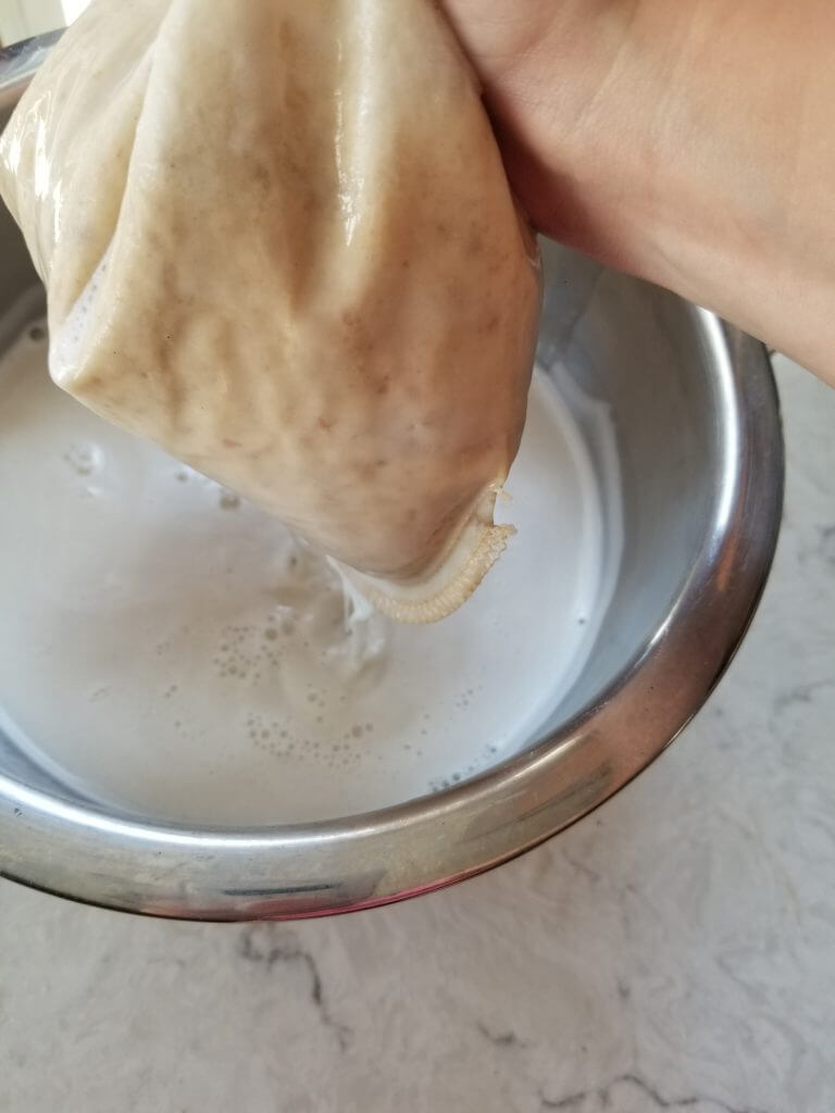 squeezing the almond milk out of the nut milk bag into a bowl