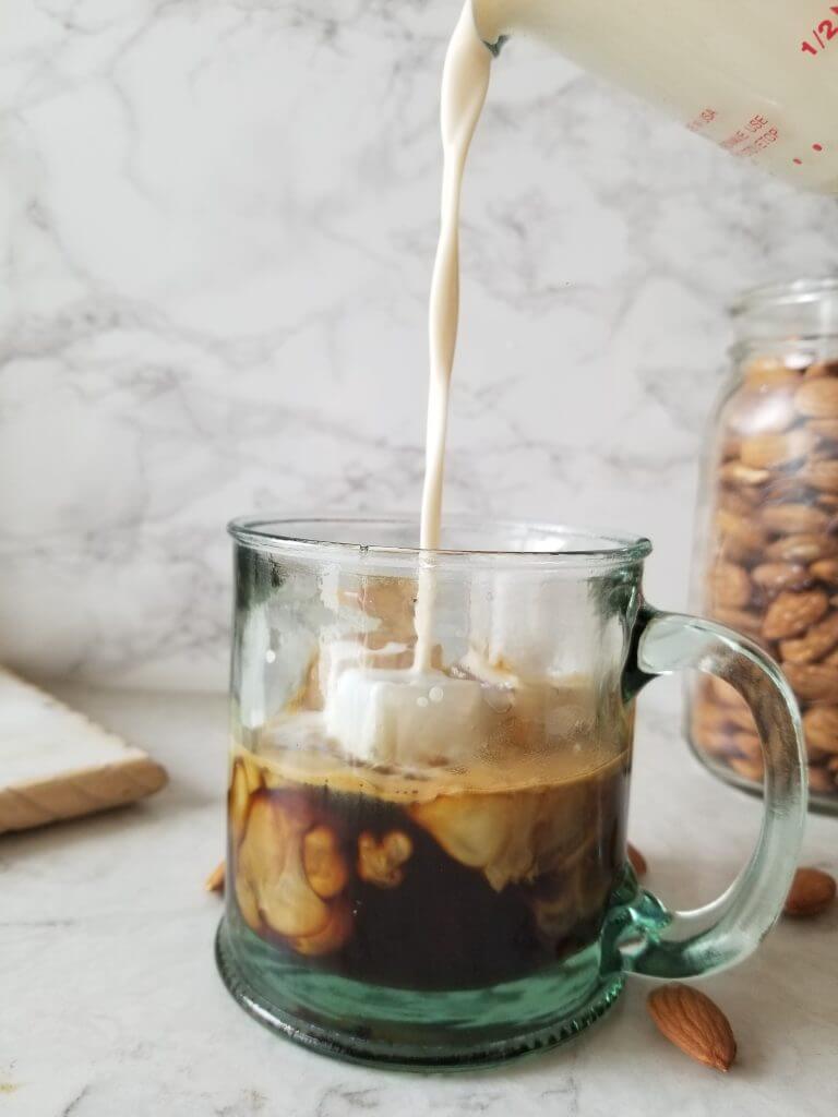 pouring Vanilla almond milk creamer into espresso in a glass