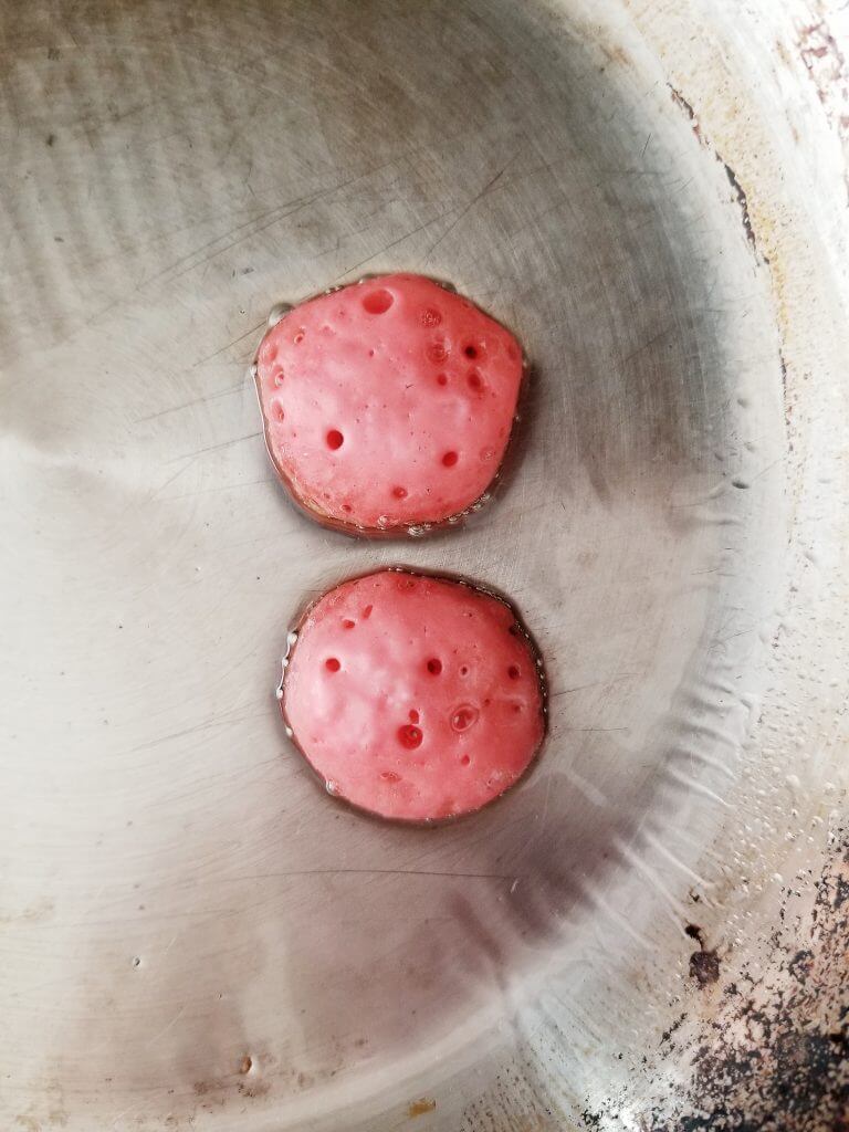 mini red pancakes with bubbles on a frying pan 